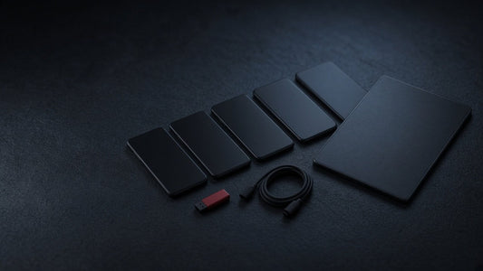 Row of smartphones and a tablet face down on a dark desk with a red USB stick and a cable